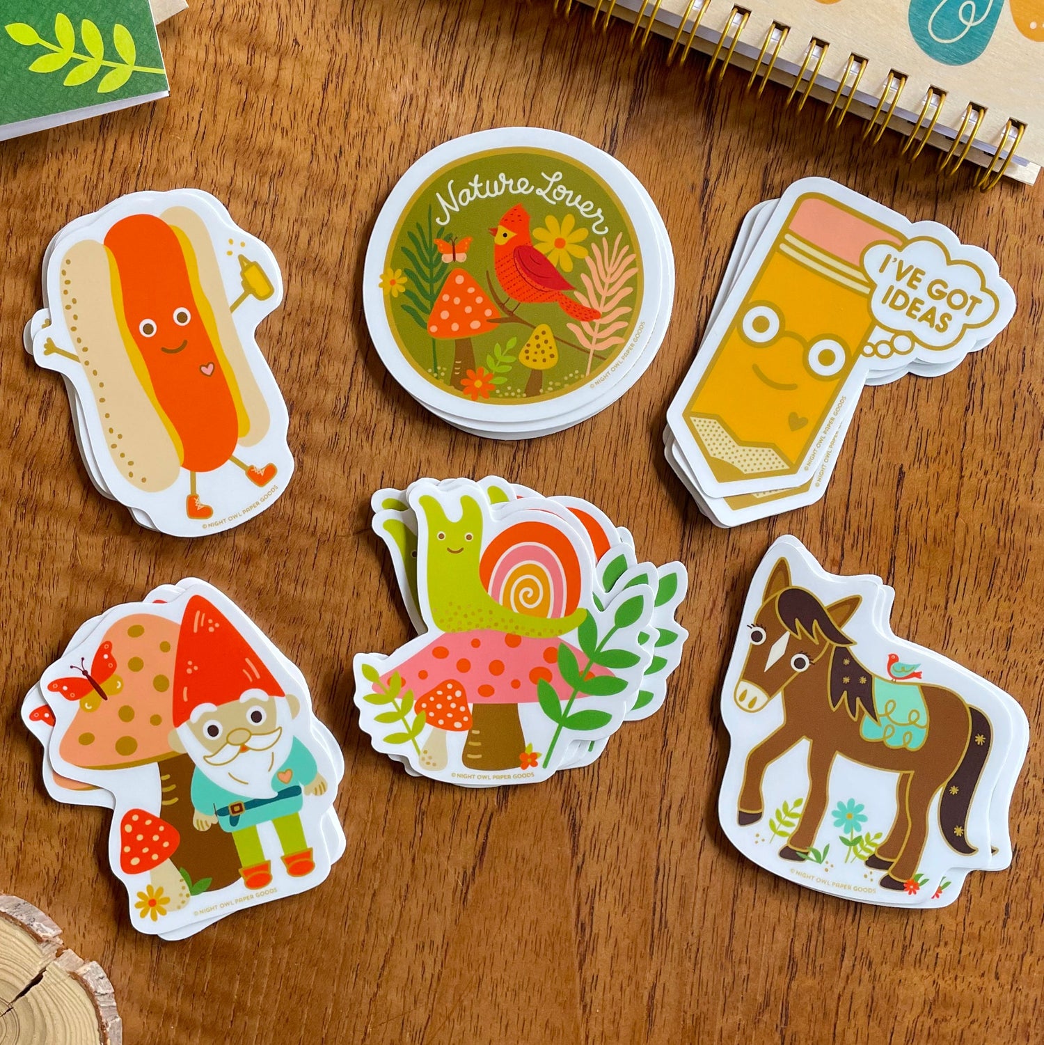 Group of cheerful, vibrant vinyl stickers, including a happy, walking hot dog, cardinal, studious pencil with happy face, gnome, snail and horse