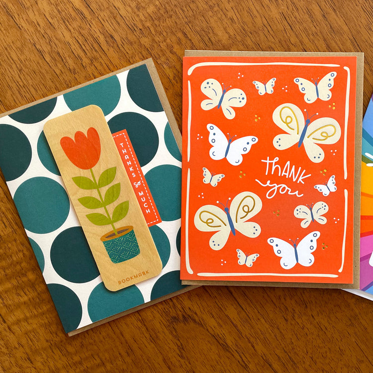 Two thank you greeting cards. One card has big dark blue polka dots with a removable wood bookmark with tall tulip. The other card is red with white and soft tan butterflies with shiny gold foil details