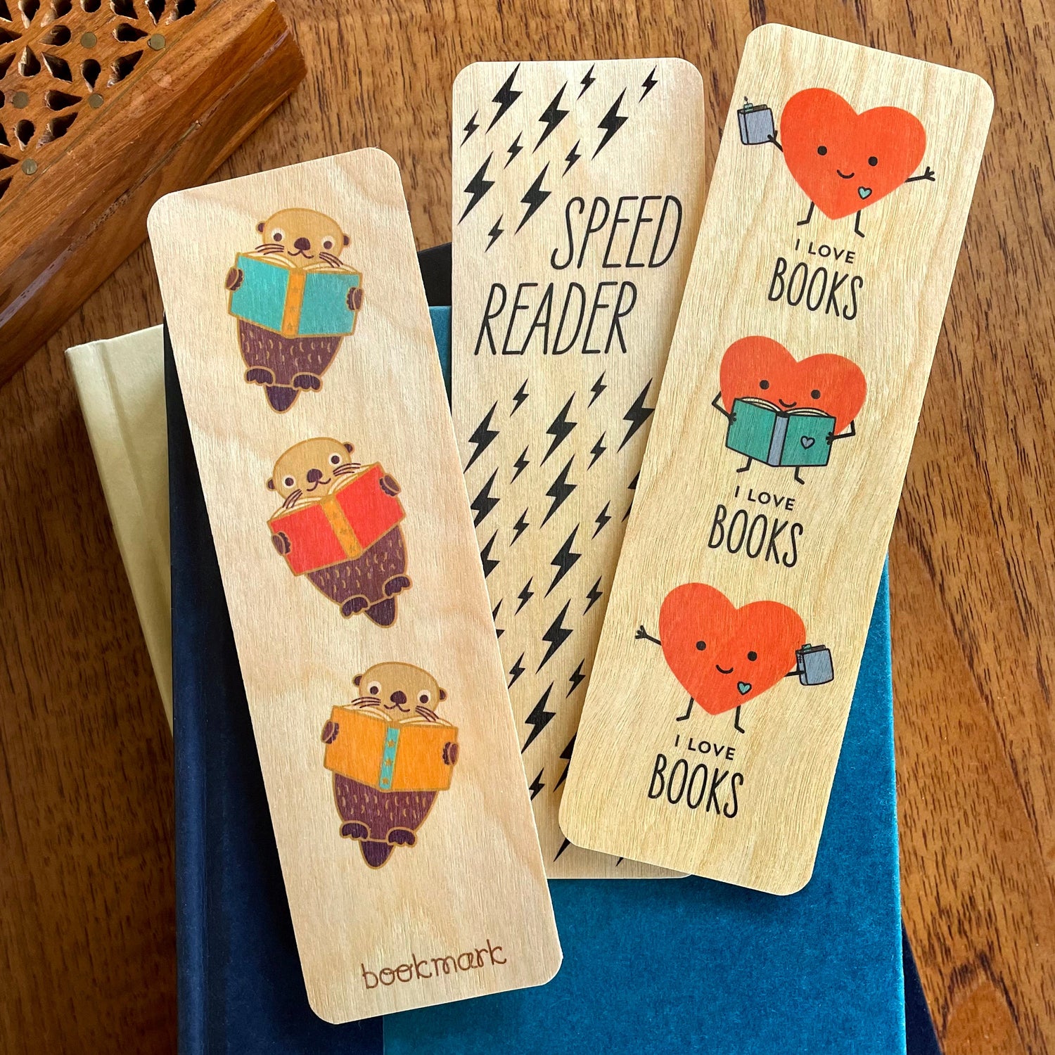 Three birch wood bookmarks in a white sweater stocking on red holiday background. Bookmarks feature a rainbow with small birch heart, black cats wearing scarfs sitting in coffee cups and smiling happy hearts holding books.