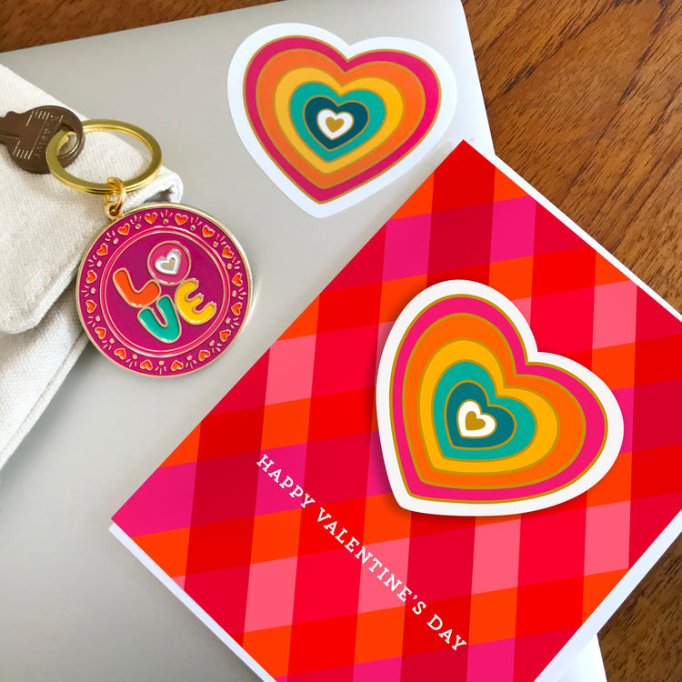 Bright red and hot pink Valentine card with removable rainbow heart sticker. Sticker shown on a laptop with a round keychain on top; tiny hearts border the circle.