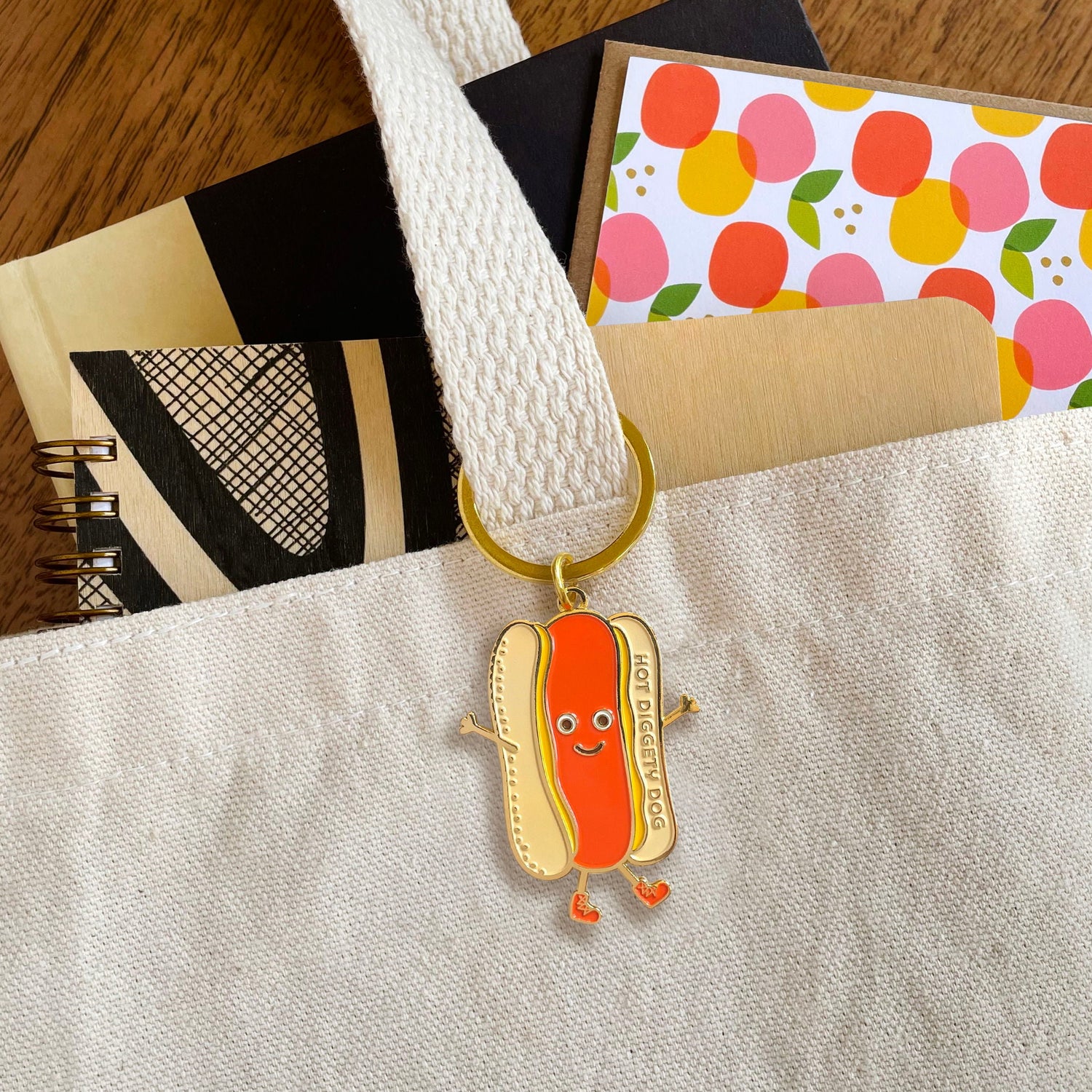 Happy hot dog key chain accessory hanging from tote bag. Fun text on key charm says 'hot diggety dog'.