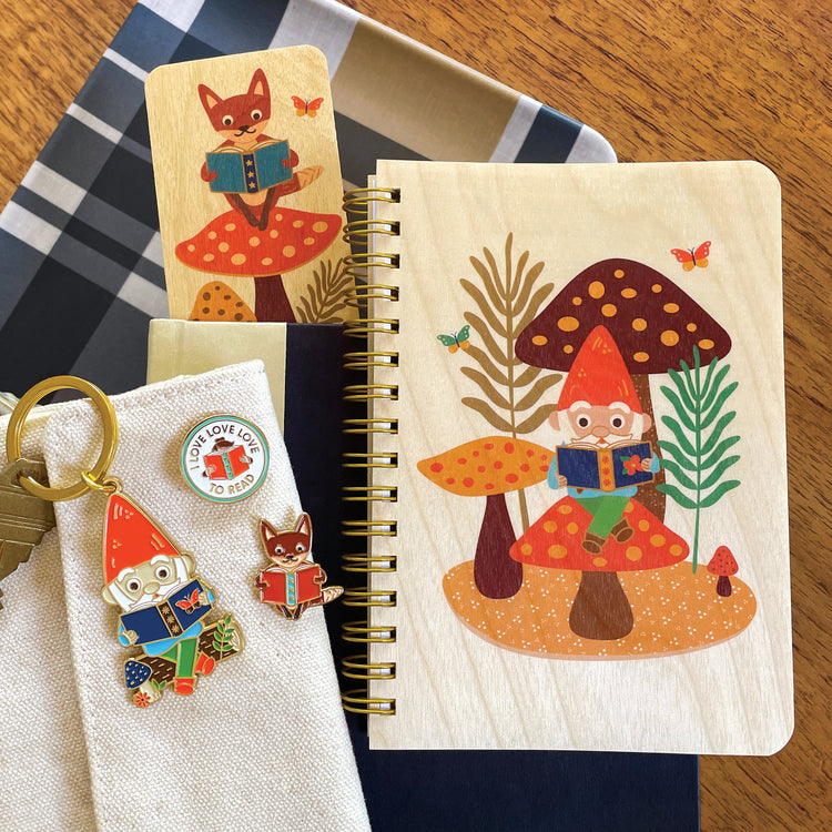 Tote bag filled with notebooks and cute book lover enamel pins with a gnome, otter, fox, mermaid, dog, tiger and also a hot dog, smiling gold heart and a beaver