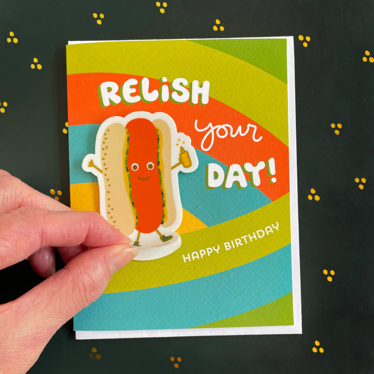 Birthday card that reads wishing you the most treemendous birthday ever with illustrated tree stump, balloons and removable vinyl beaver sticker. shows hand lifting up sticker