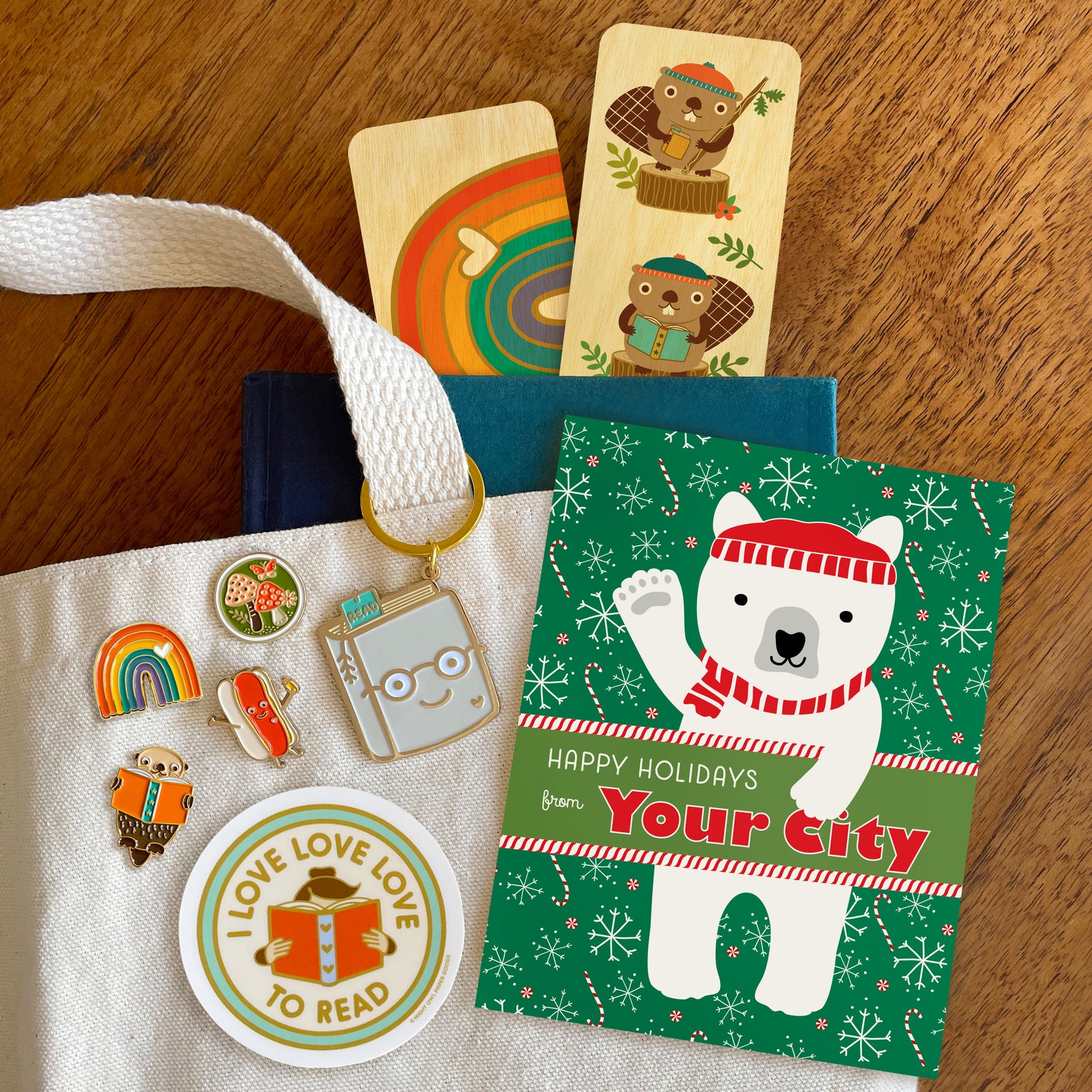 Assortment of products including enamel pins, keychains, stickers, bookmarks and a customizable holiday card.