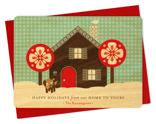 Customizable birch wood holiday card with a printed walnut wood grain house, dog, snowy sky, "Happy Holidays from our Home to Yours" text and a personal greeting. Shown with a red envelope.