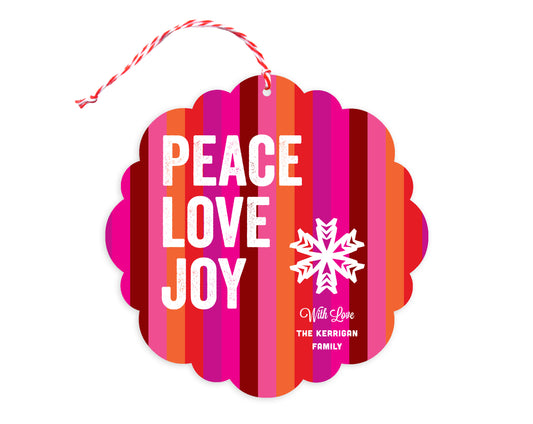 Front of customizable paper holiday ornament card featuring bright, colorful stripes, "Peace Love Joy" text, a snowflake and a personal message. Round ornament with scalloped edges.