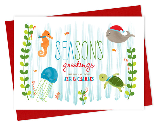 Front of personalized paper holiday card with cute marine sea creatures, "Season's Greetings" text and a personalized message on a white background. Shown with a red envelope. 