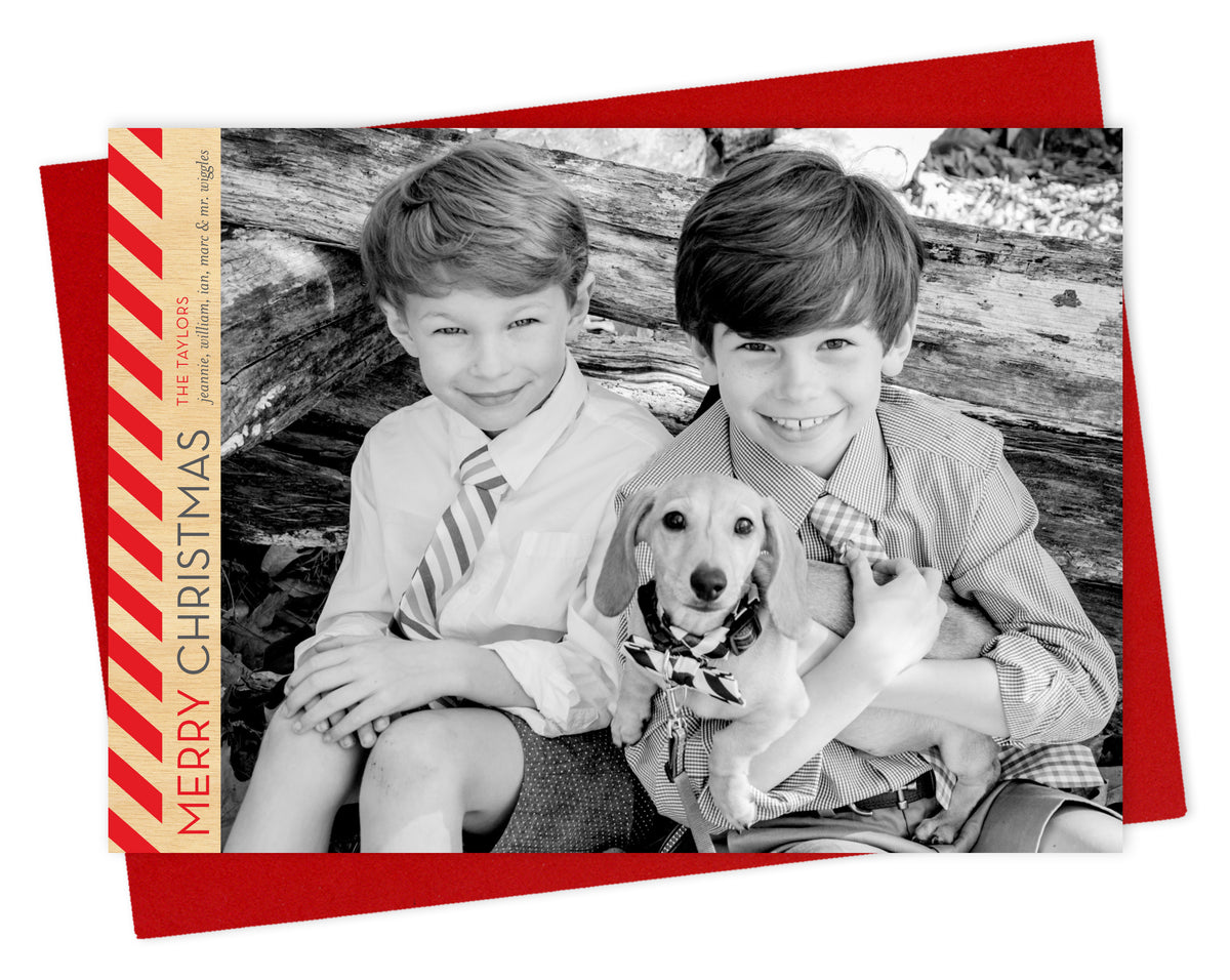 Customizable paper holiday card featuring a landscape photo with bold diagonal red stripes, “MERRY CHRISTMAS” text and a personal greeting running vertically along the left side. Shown with a red envelope.