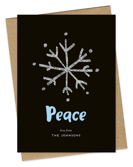 Customizable wood holiday card featuring a large illustrated snowflake, aqua "Peace” text and a personal greeting against a rich black backdrop. Shown with a kraft envelope.