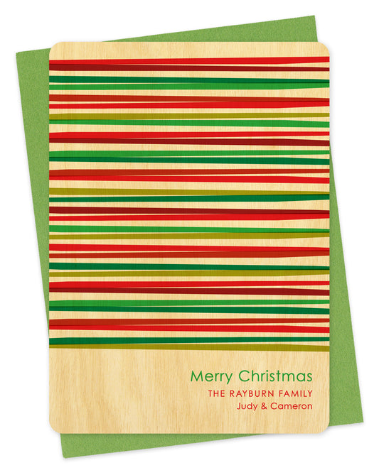 Customizable birch wood Christmas card with horizontal stripes in various shades of red and green and a personal greeting. Shown with a green envelope.