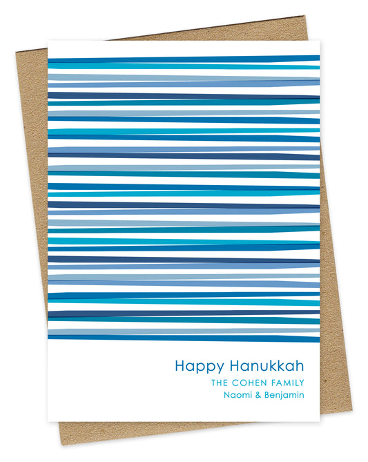 Customizable paper Hanukkah card featuring vibrant blue interwoven stripes, “Happy Hanukkah” text and a personal greeting on a white background. Shown with a kraft envelope.