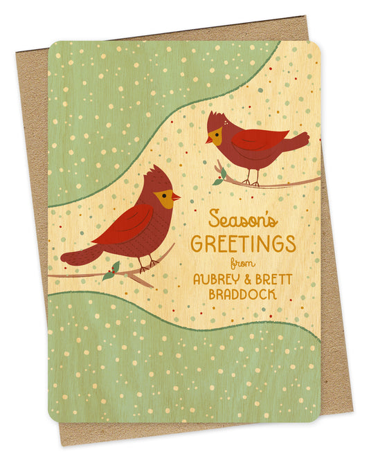 Customizable birch wood Christmas card featuring two red cardinals perched against a snowy background with “Season’s Greetings” text and a personal greeting. Shown with a kraft envelope.