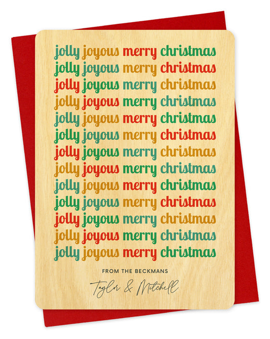 Customizable birch wood holiday card featuring cheerful, multicolored “Jolly Joyous Merry Christmas” text repeated down the length of the card and a personal greeting at the bottom. Shown with a red envelope.