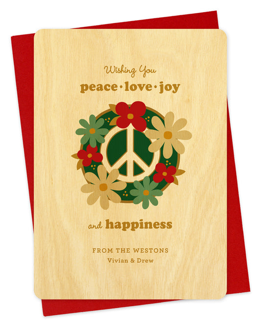 Customizable birch wood holiday card featuring a bold peace sign decorated with festive florals, a “Wishing you peace, love, joy and happiness” text and a personal greeting. Shown with a red envelope.