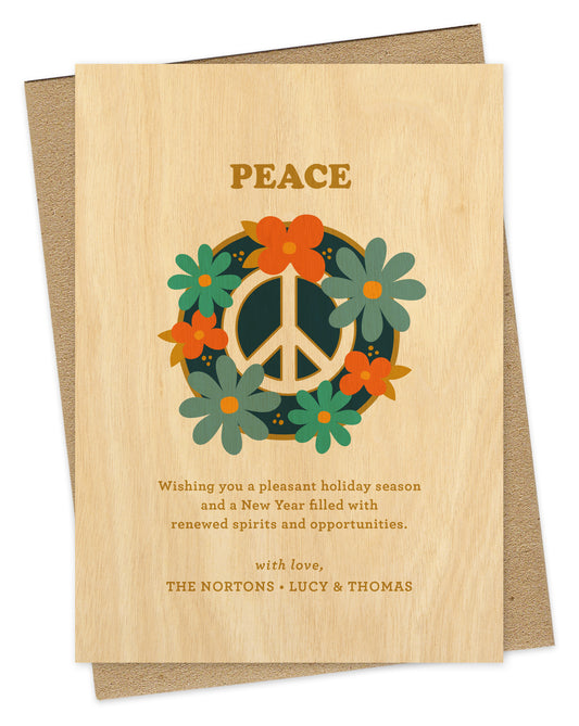 Customizable paper holiday card with a printed birch wood grain background. Card design features a peace sign surrounded by colorful flowers with “Peace” text at the top and a personal greeting at the bottom. Shown with a kraft envelope.