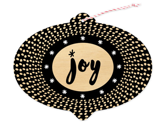 Front of bulb-shaped paper holiday ornament card with black-and-white pattern and “Joy” greeting on a printed birch wood background.