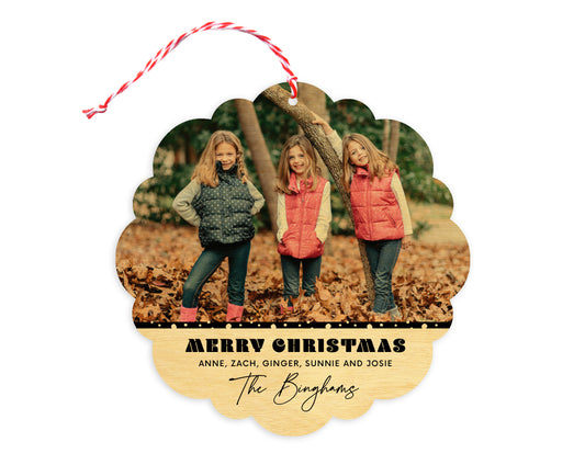 Front of customizable birch wood holiday ornament card featuring a photo with a snowy black border, “Merry Christmas” text and a personal message. Round ornament with scalloped edges.