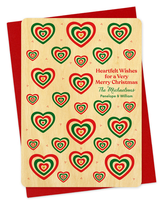 Customizable birch wood Christmas card with red and green heart patterns and a personal greeting. Shown with a red envelope.