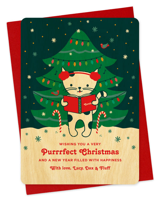 Customizable birch wood holiday card featuring a cute cat caroling in front of a decorated outdoor Christmas tree, "Wishing you a Very Purrrfect Christmas" text and a personal greeting at the bottom. Shown with a red envelope.
