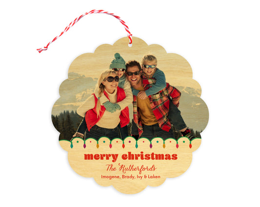 Front of customizable birch wood holiday ornament card featuring a photo with a festive Christmas lights border, “Merry Christmas” text and a personal message. Round ornament with scalloped edges.