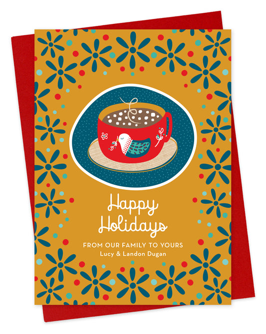 Front of paper holiday card featuring a mug of hot chocolate with a folk-style bird design, “Happy Holidays” text and a  personal greeting on a festive patterned background. Shown with a red envelope.