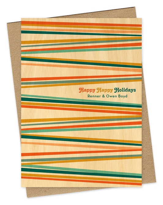 Customizable paper Christmas card with colorful stripes in bright shades of blue, orange and gold, "Happy Happy Holidays" text and a personal greeting, all on a printed birch wood grain background. Shown with a kraft envelope.