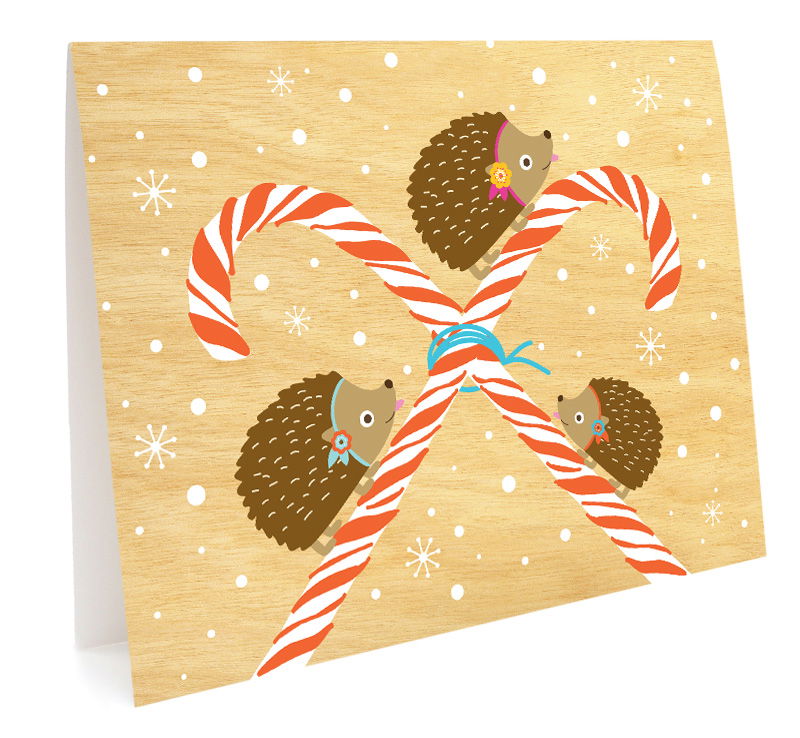Peppermint Hedgies folded paper holiday card featuring three hedgehogs climbing crossed candy canes against a warm birch wood-printed background with snowflakes and dots