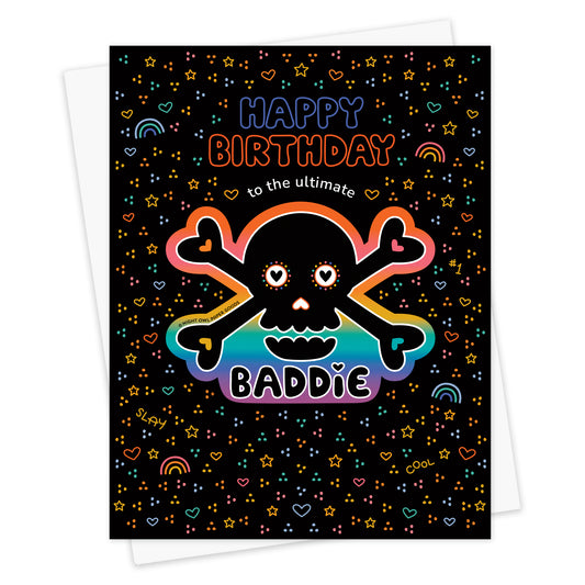 Front of birthday greeting card with a removable rainbow skull vinyl sticker and "Happy Birthday to the Ultimate Baddie" text surrounded by colorful rainbow, star, and heart designs on a black background. Shown with a white envelope.
