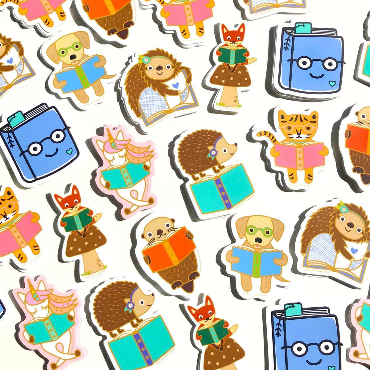 Array of book lover stickers, including a reading golden retriever, a reading sloth, a reading unicorn, a reading otter, a hedgehog standing on a book, an otter holding a book, a reading tiger and a happy book wearing glasses.