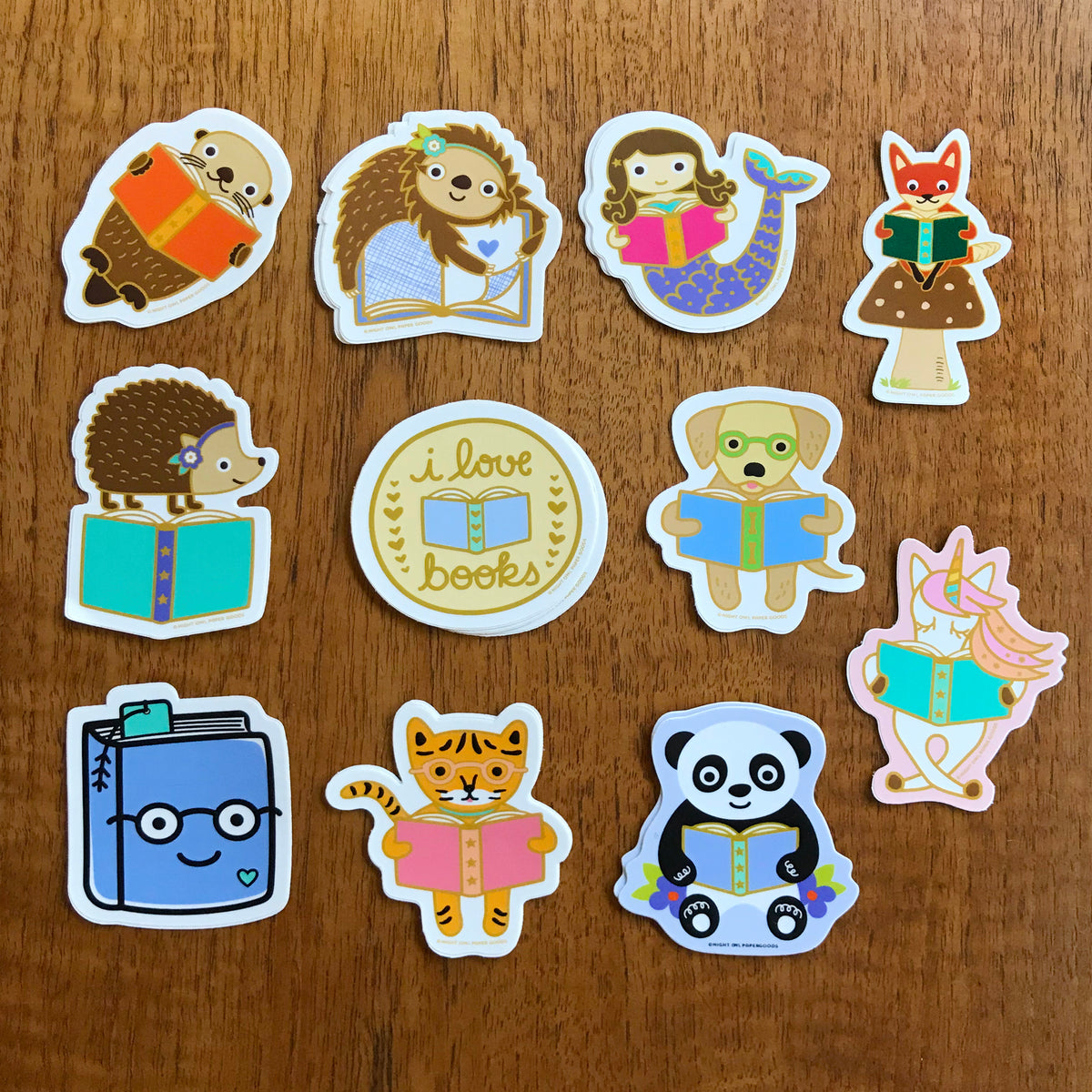 11 book lover stickers, including a reading golden retriever, a reading sloth, a reading unicorn, a reading otter, a hedgehog standing on a book, an otter holding a book, a reading tiger, a mermaid holding a book, a reading panda bear, a happy book wearing glasses and a round sticker that features an open book and "I love books" text.