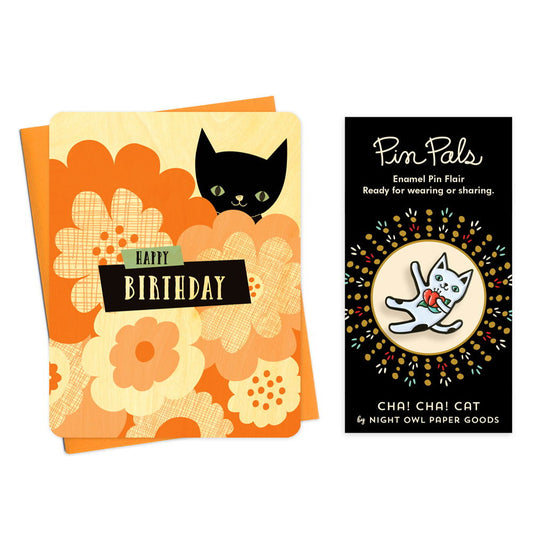 Wood birthday card with black cat and floral design and "Happy Birthday" text alongside an enamel pin of a white cat with black spots holding a red flower.