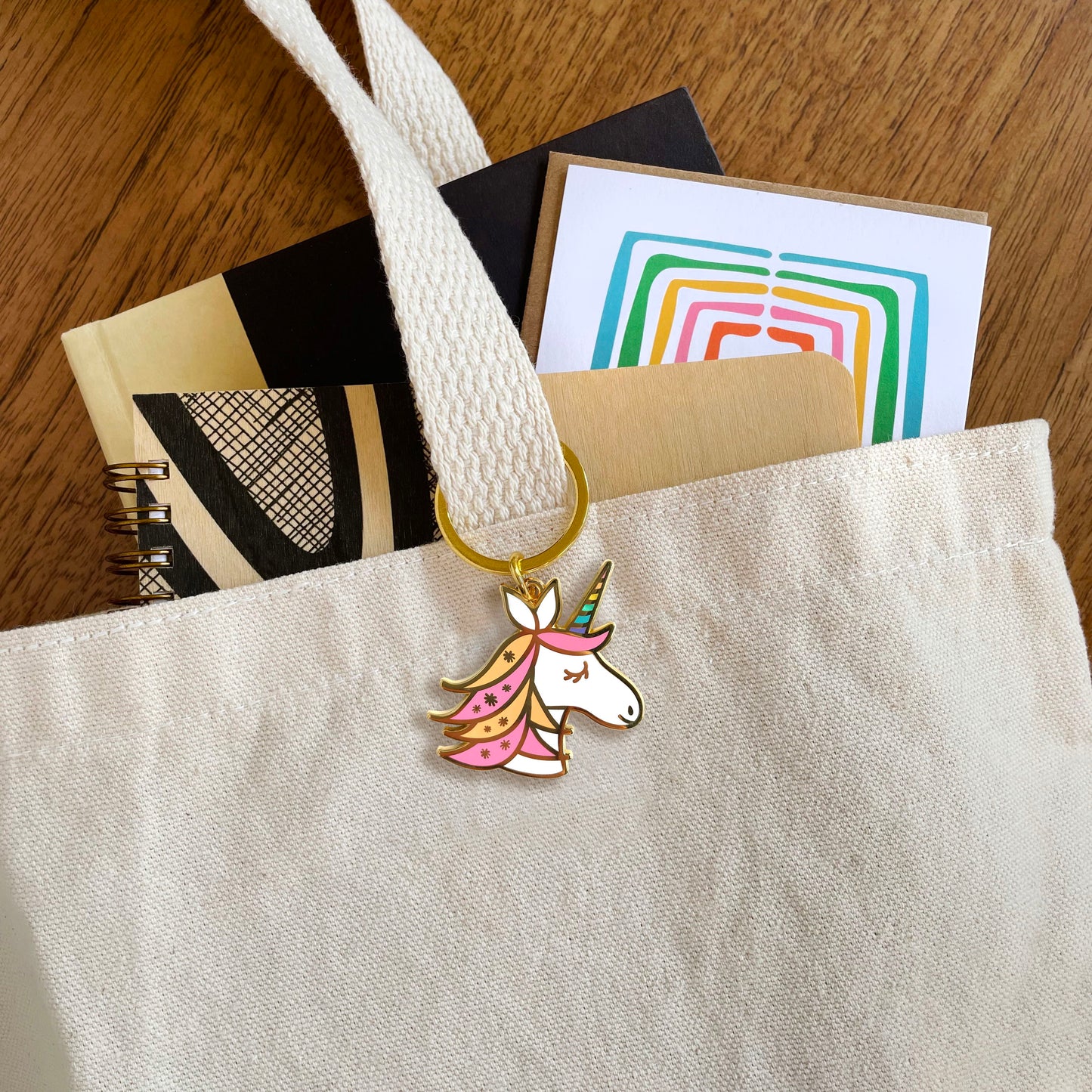 Unicorn enamel keychain hanging from a tote bag handle