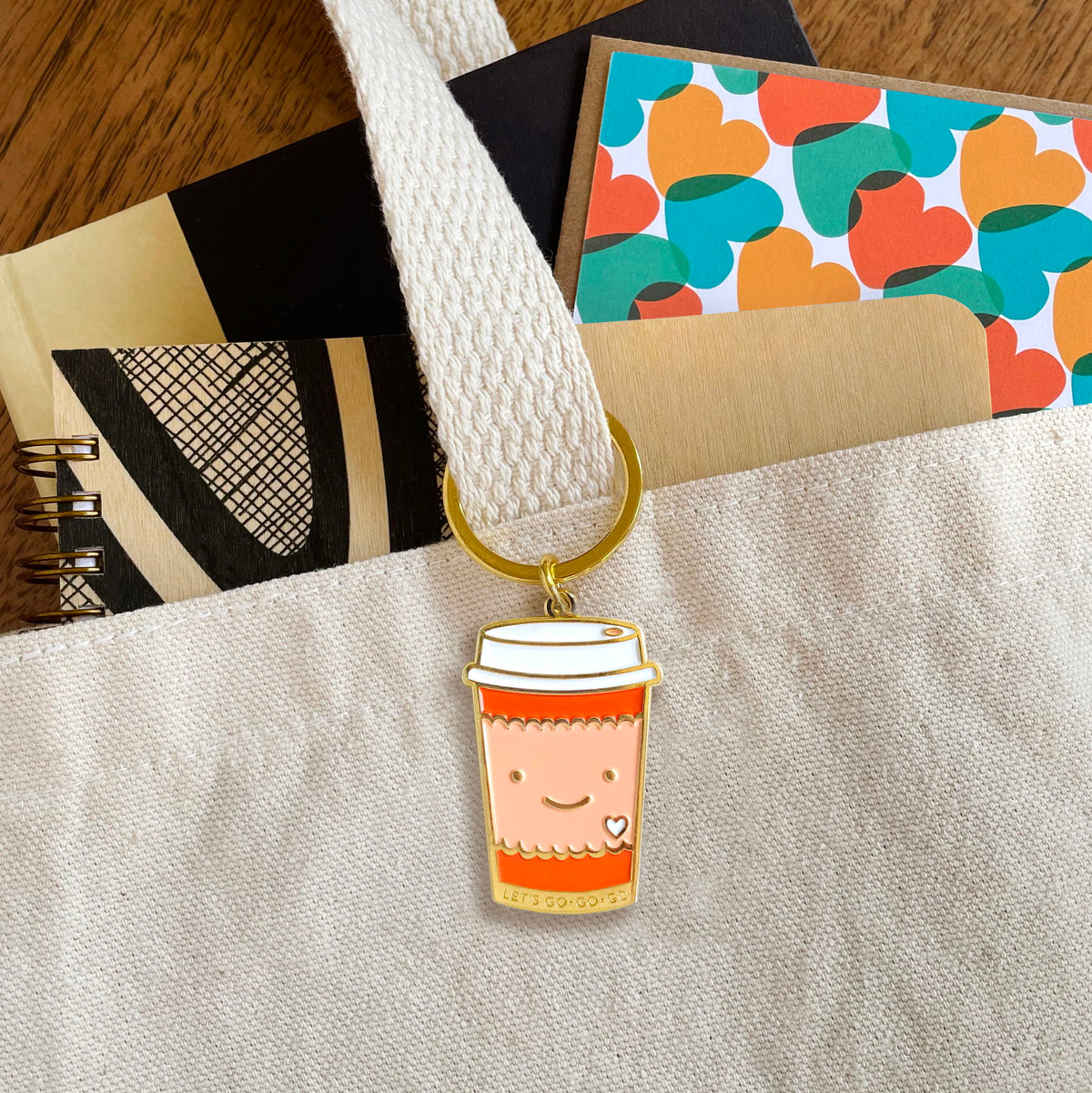 Coffee to go enamel keychain hanging from a tote bag handle