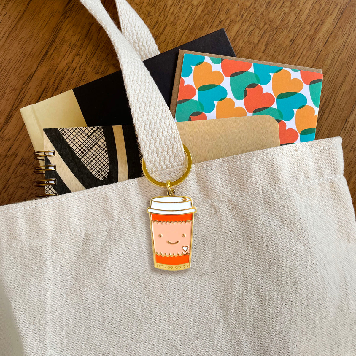 Coffee to go enamel keychain hanging from a tote bag handle