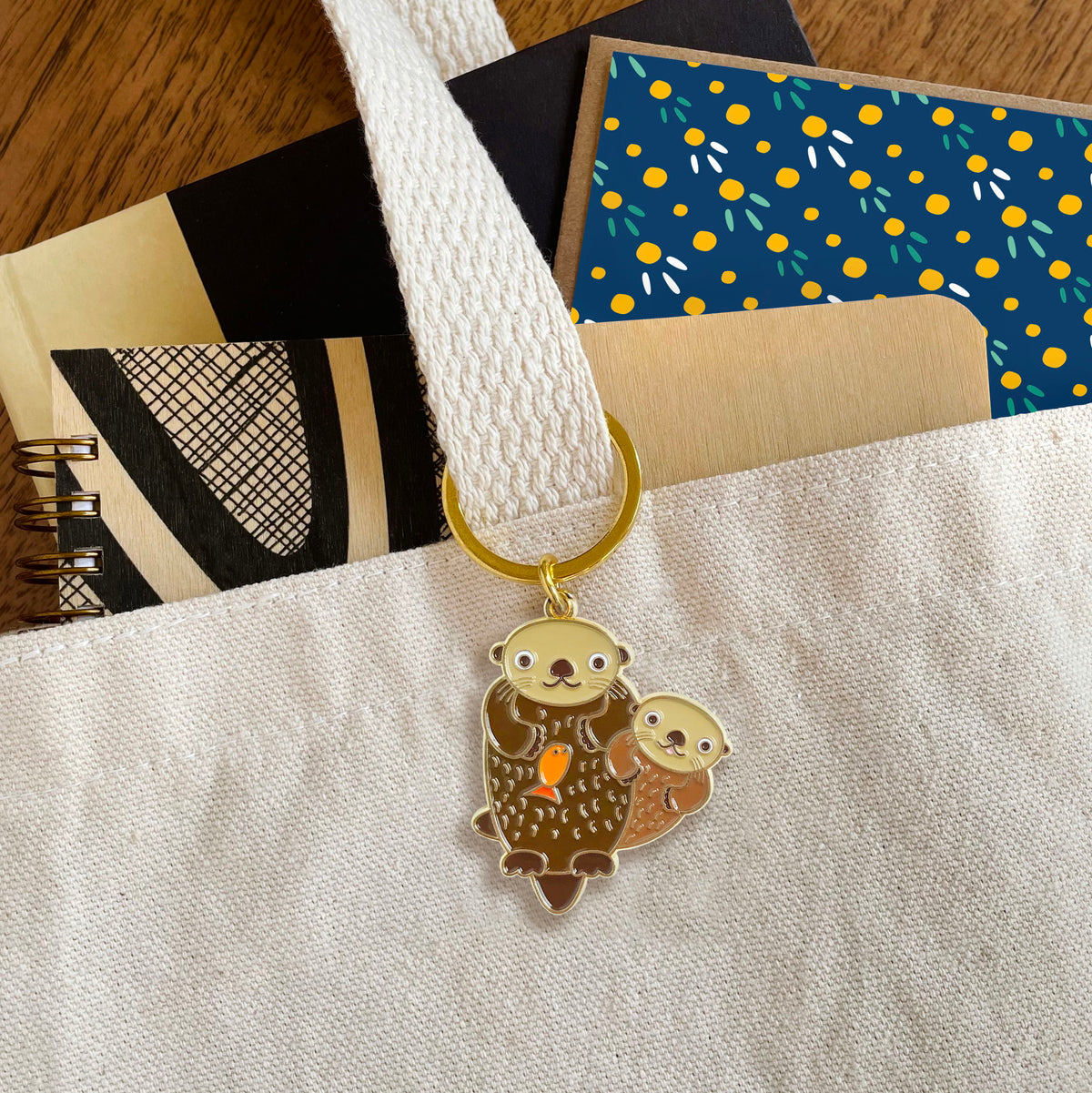 Otter enamel keychain hanging from a tote bag handle