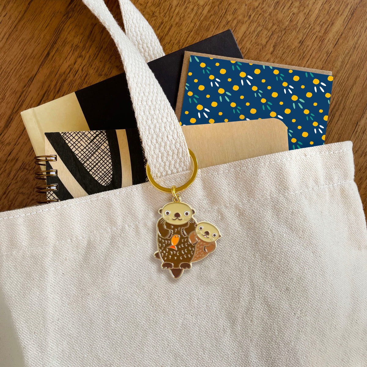Otter enamel keychain hanging from a tote bag handle