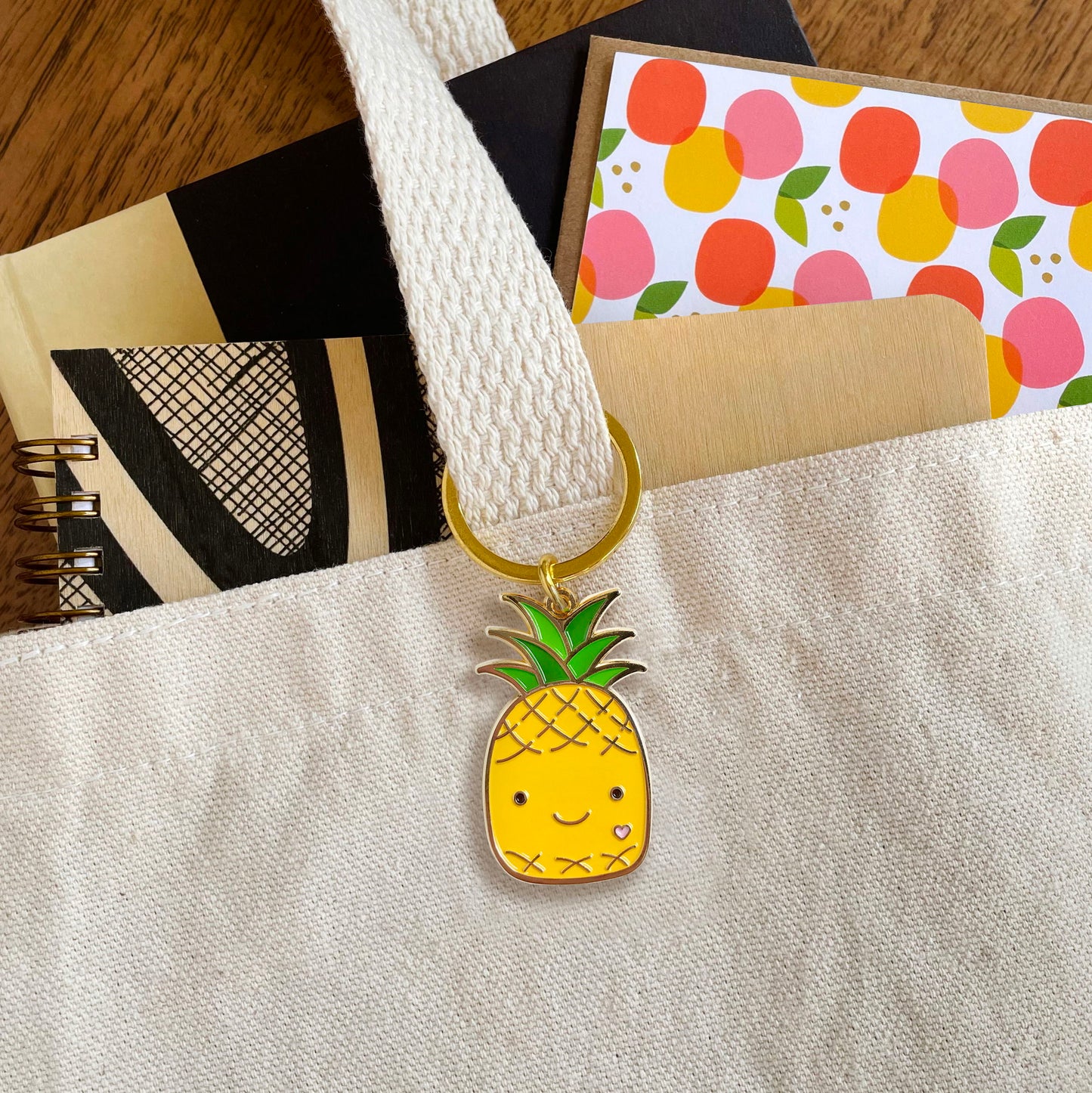 Happy Pineapple enamel keychain hanging from a tote bag handle