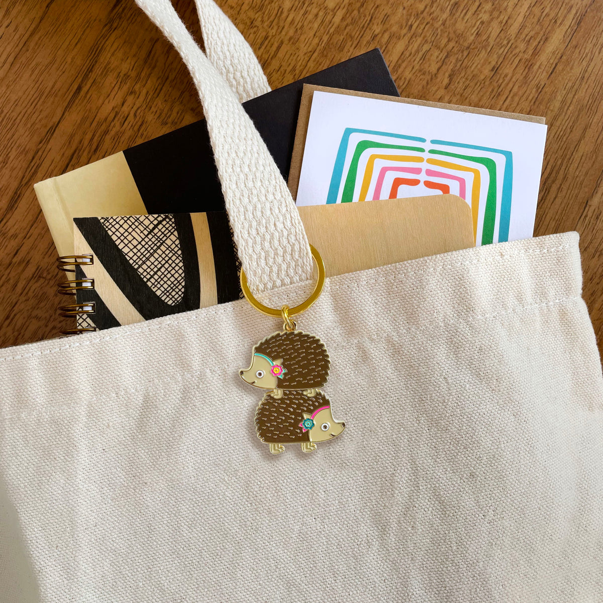 Stacked Hedgehogs enamel keychain hanging from a tote bag handle