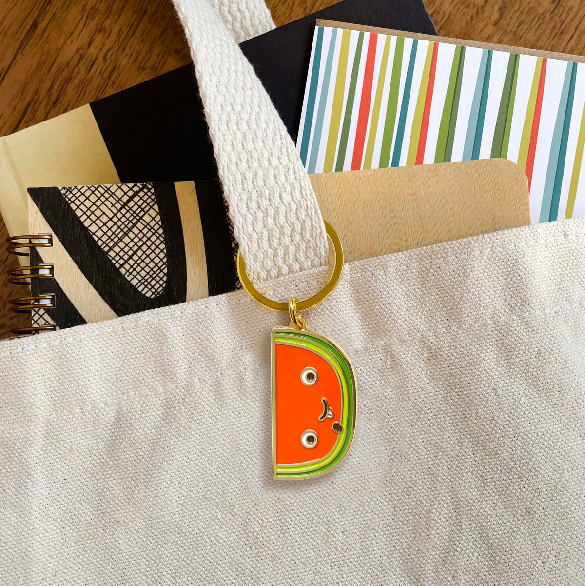 Watermelon slice enamel keychain hanging from a tote bag handle