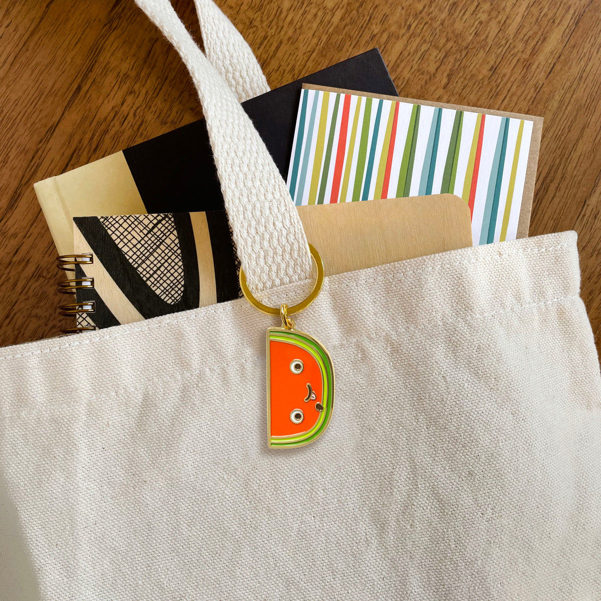 Watermelon slice enamel keychain hanging from a tote bag handle