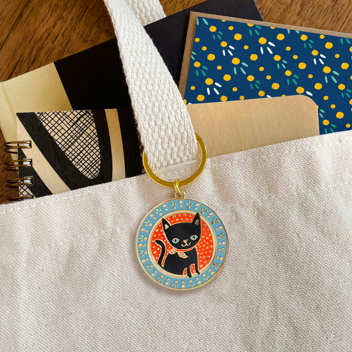 Black cat enamel keychain hanging from a tote bag handle