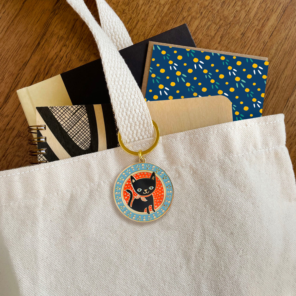 Black cat enamel keychain hanging from a tote bag