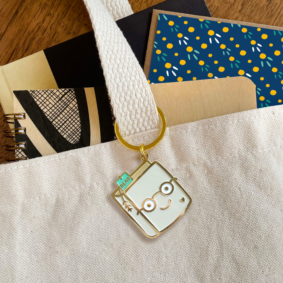 Book Lover enamel keychain hanging from a tote bag handle