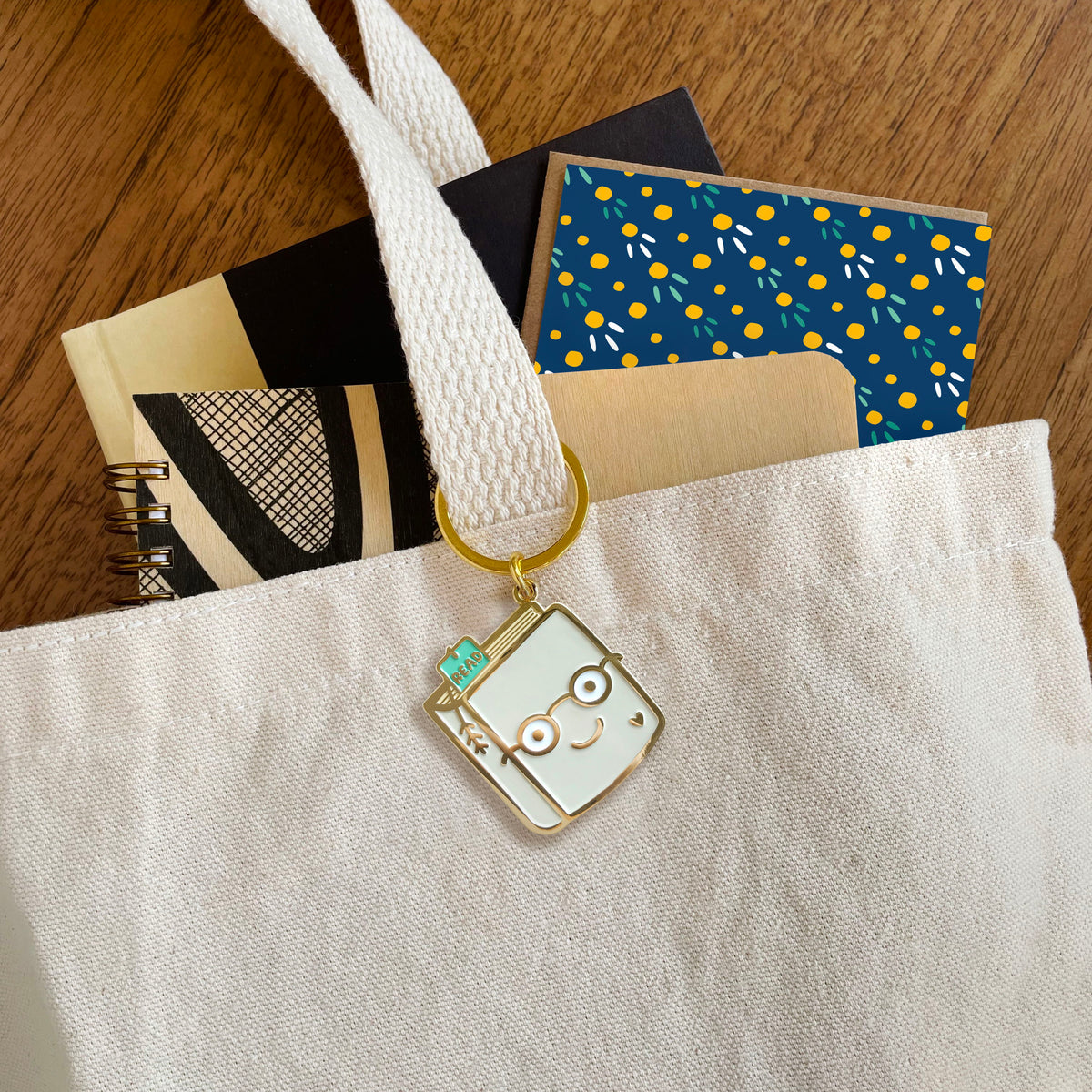 Book Lover enamel keychain hanging from a tote bag handle