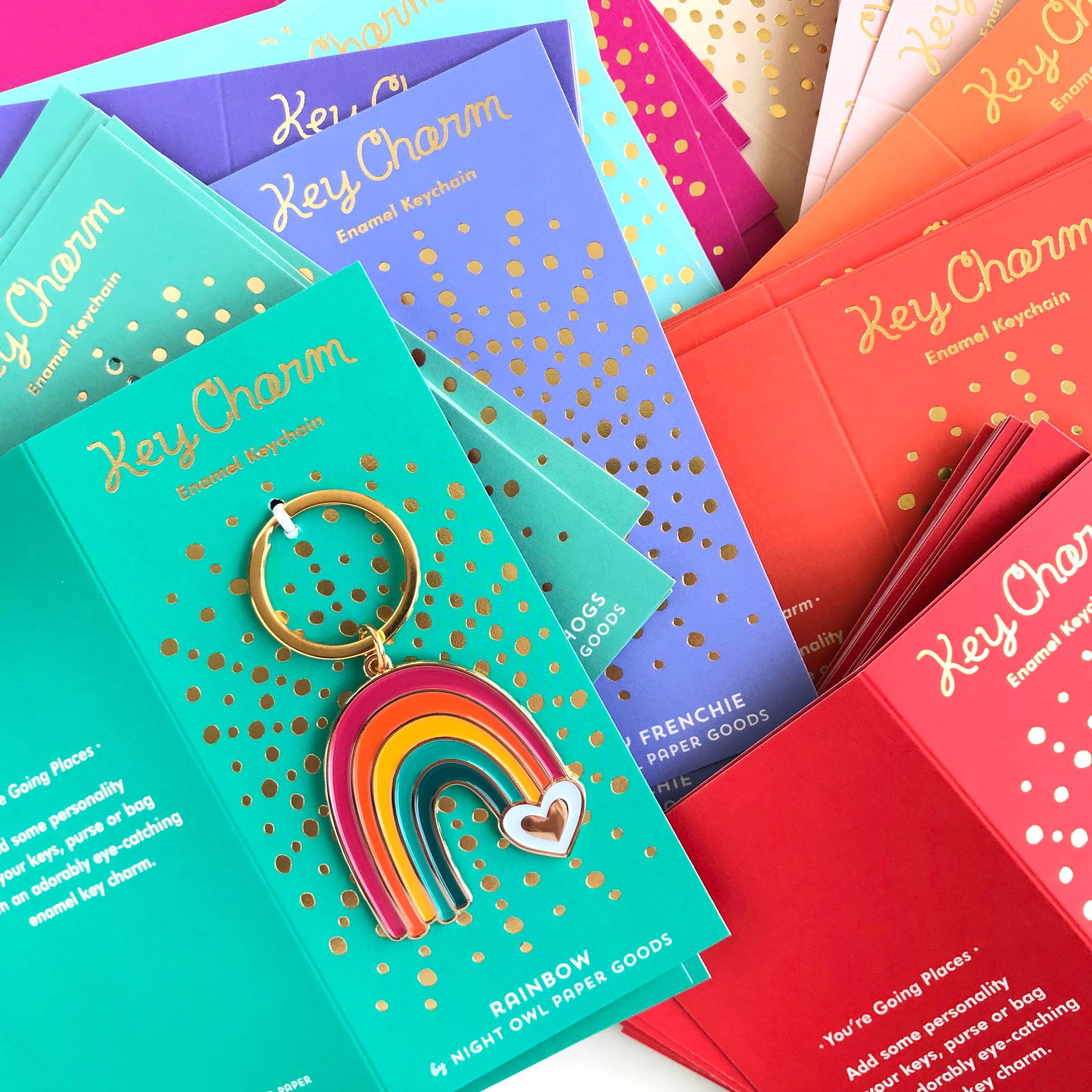 Rainbow enamel keychain on gold foil stamped backer card. Backer card is aqua and reads "Key Charm Enamel Keychain" at top and "Rainbow by Night Owl Paper Goods" at bottom.