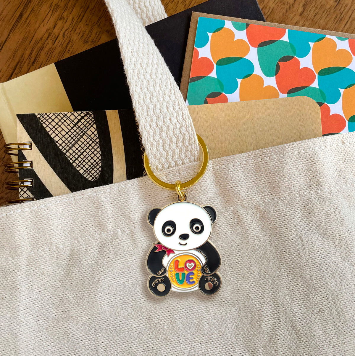 Panda enamel keychain hanging from a tote bag handle