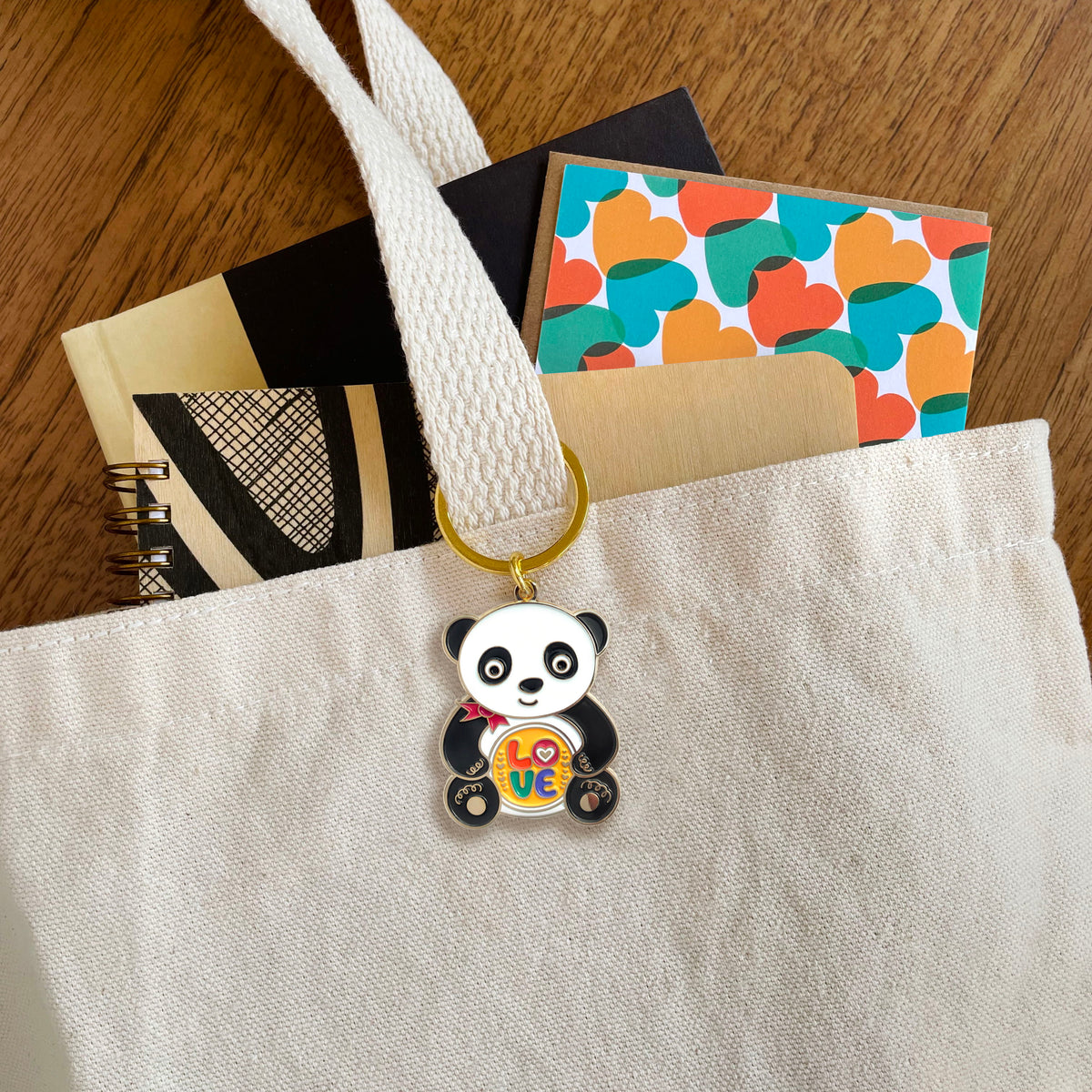 Panda enamel keychain hanging from a tote bag handle