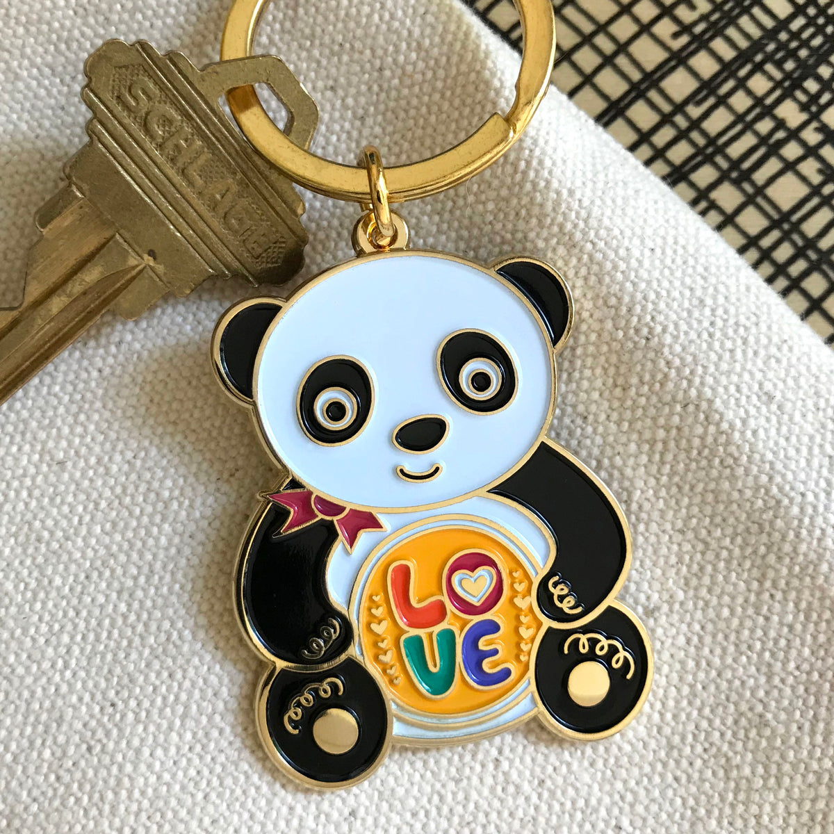 Gold metal panda enamel keychain featuring a black and white panda with a red bow holding a colorful "LOVE" sign on a gold key ring