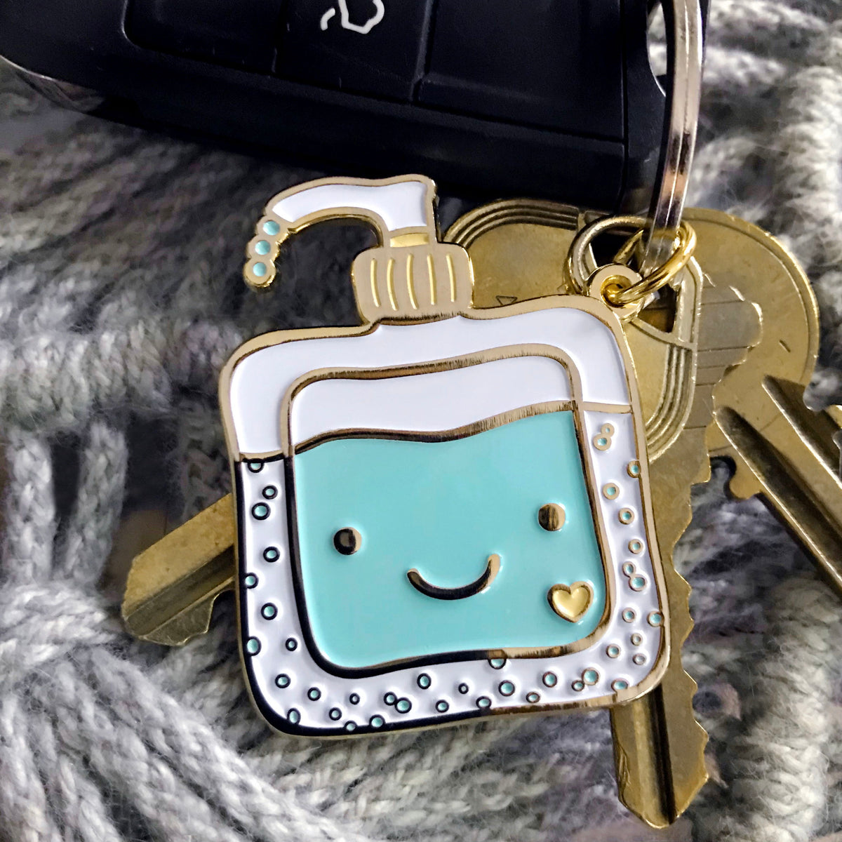 Gold metal hand sanitizer enamel keychain featuring a smiling aqua sanitizer bottle with heart detail on a gold key ring