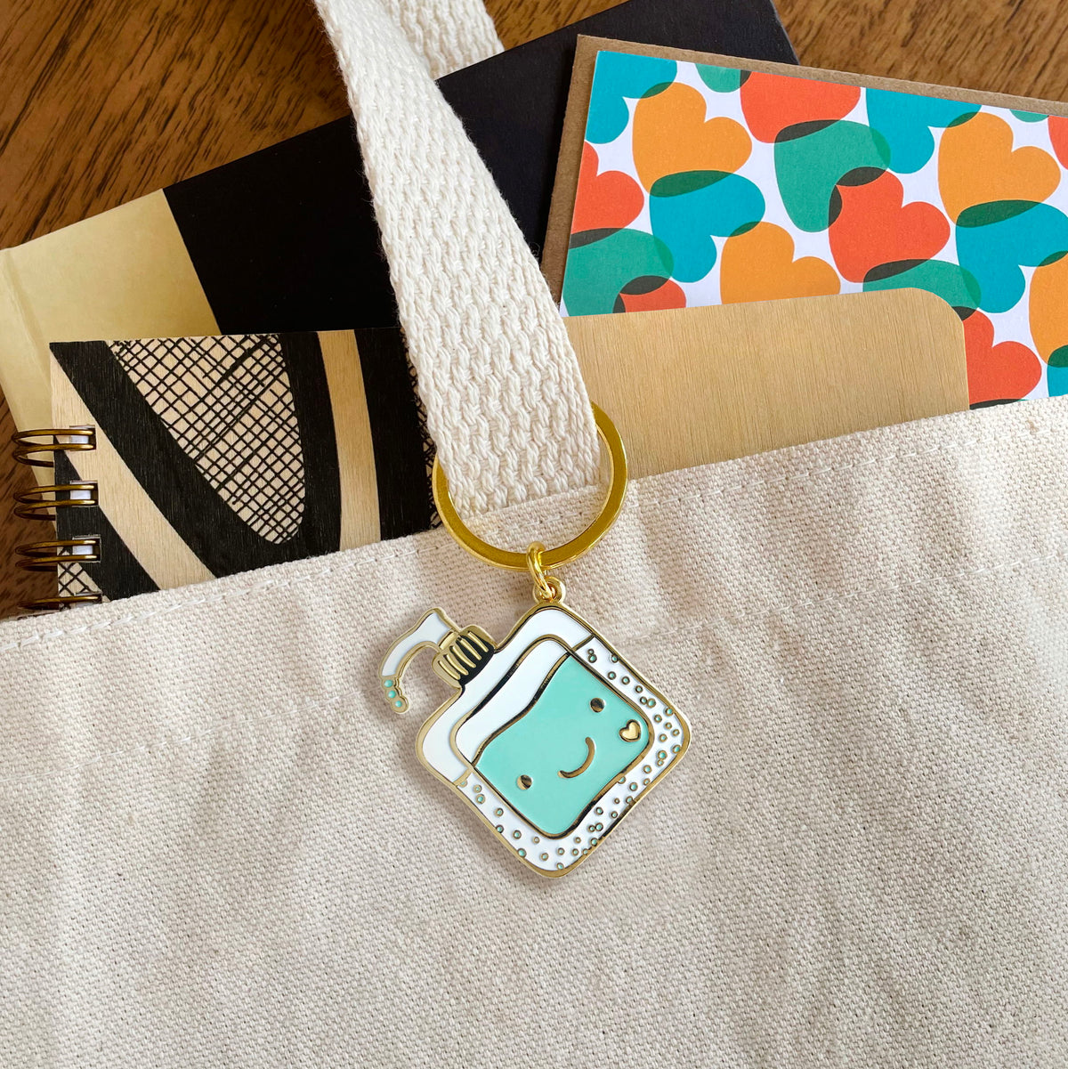 Happy Hand Sanitizer enamel keychain hanging from a tote bag handle
